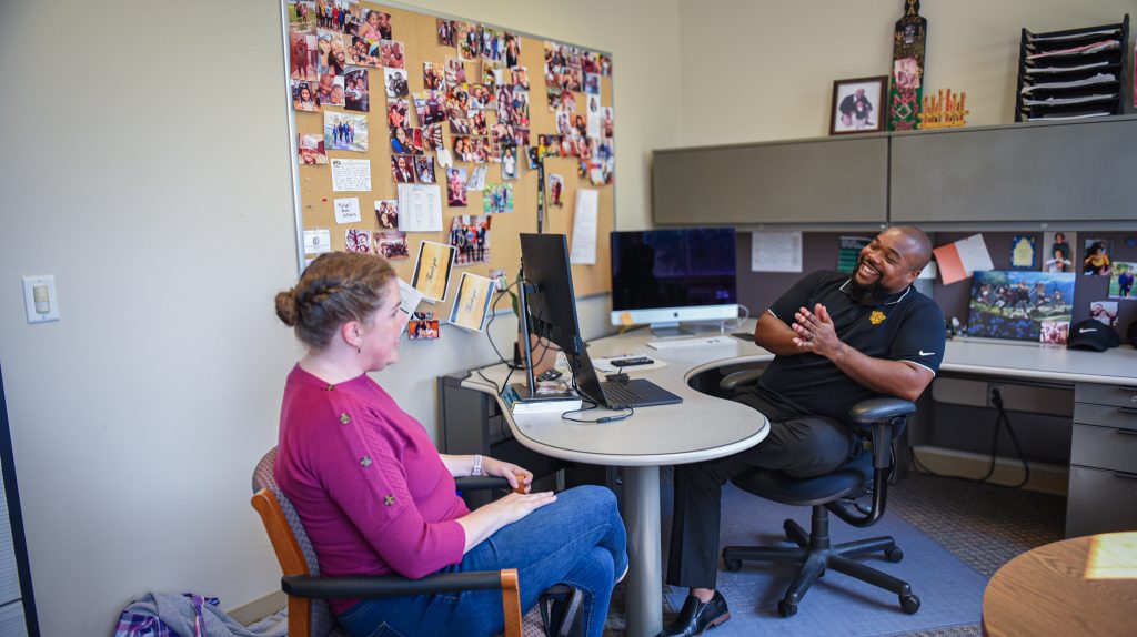 Michael S. Williams, Ph.D., assistant professor in the College of Education sitting at desk in office talking to Amanda Carr, doctoral candidate.