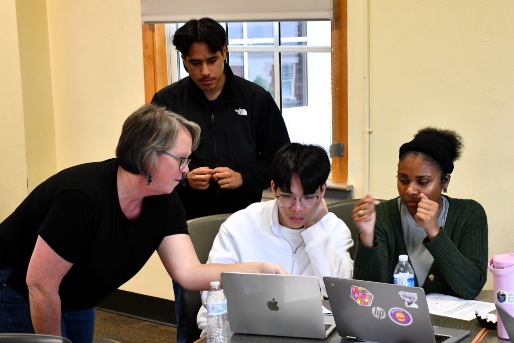 Dr. Carolyn Orbann pointing to the laptop screen of a male student while two other students (male and female) look on