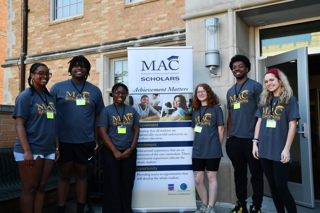 Six college students stand for a group photo with a vertical program banner