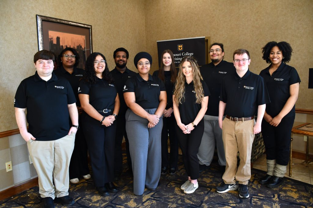 Small group of adults in uniform polos pose in front of a program banner