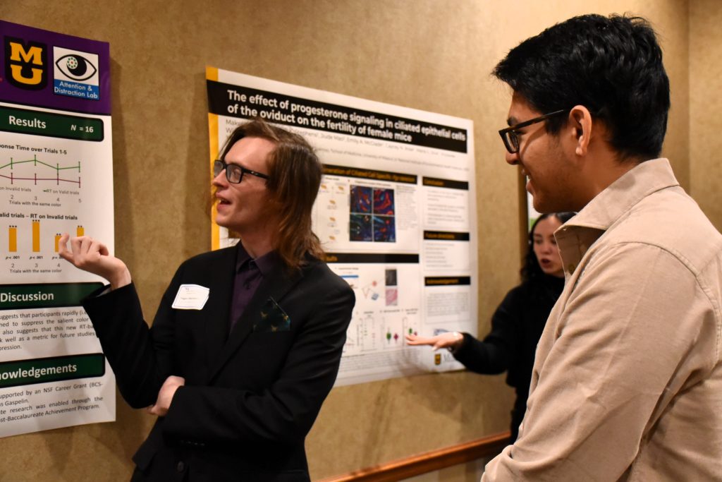 scholar presenting research poster to a onlooking adult